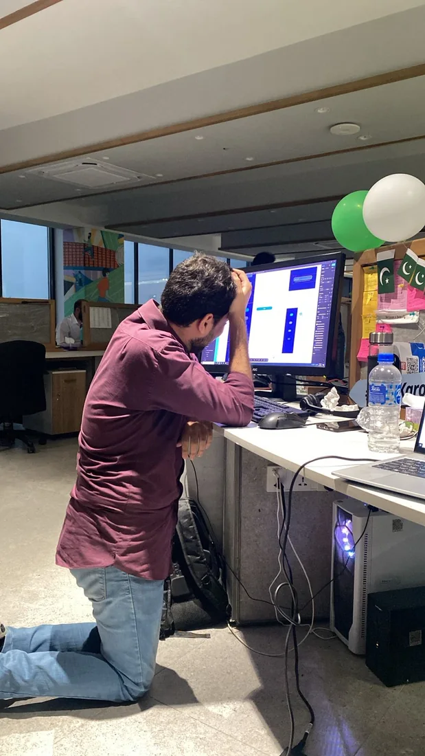 Behind the scenes: a teammate leaning against a desk with a hand on their head, facing a monitor