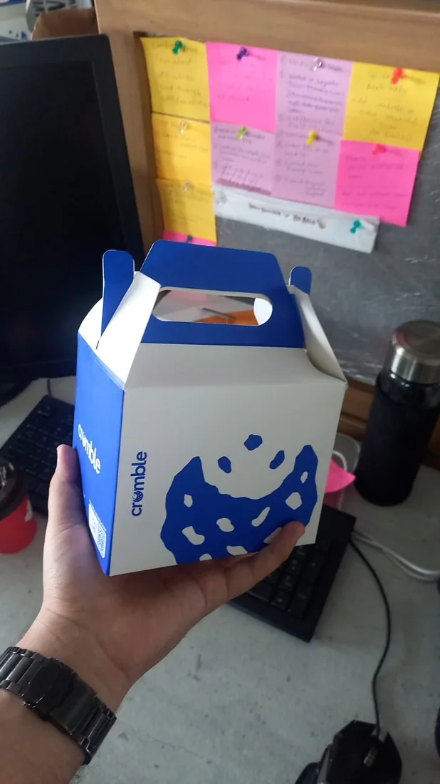 Behind the scenes: a hand holding a takeaway box of cookies in front of a wall of sticky notes